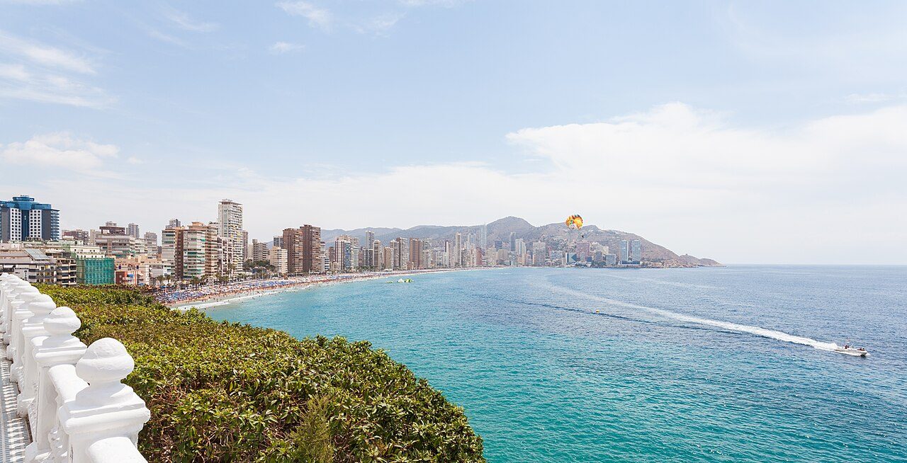 Vista de la bahía de Benidorm con una larga playa y una línea continua de rascacielos junto al mar azul turquesa.
