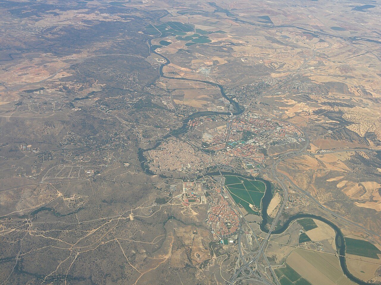 Vista aérea de Toledo: el casco antiguo compacto dentro de una curva cerrada del río Tajo y, alrededor, barrios modernos, campos y carreteras