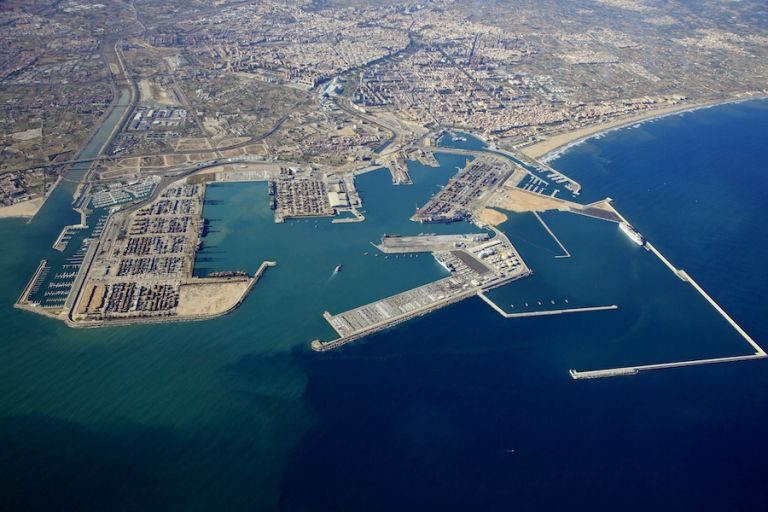 Vista aérea del puerto de Valencia con sus muelles y explanadas llenas de contenedores apilados, la ciudad al fondo y el mar Mediterráneo delante
