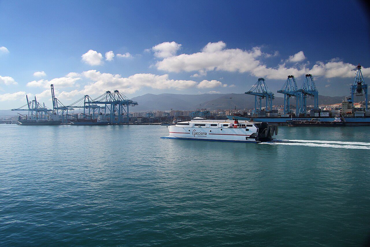 Bahía de Algeciras con grandes grúas pórtico de contenedores junto a los muelles y un ferri blanco navegando en primer plano