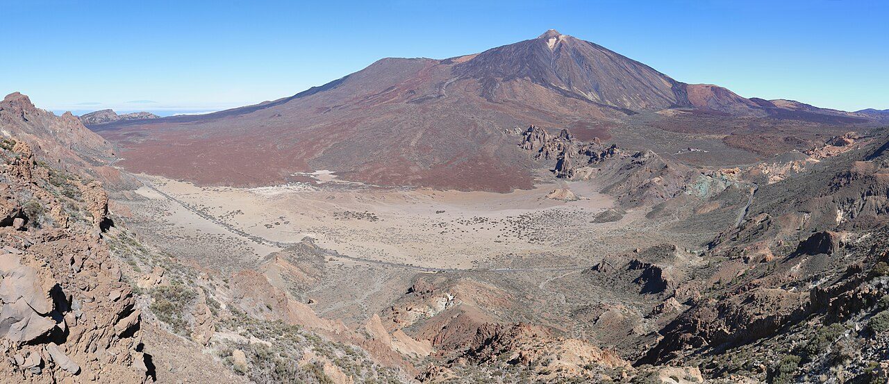 Panorámica de una llanura volcánica con coladas oscuras y, detrás, el cono del Teide
