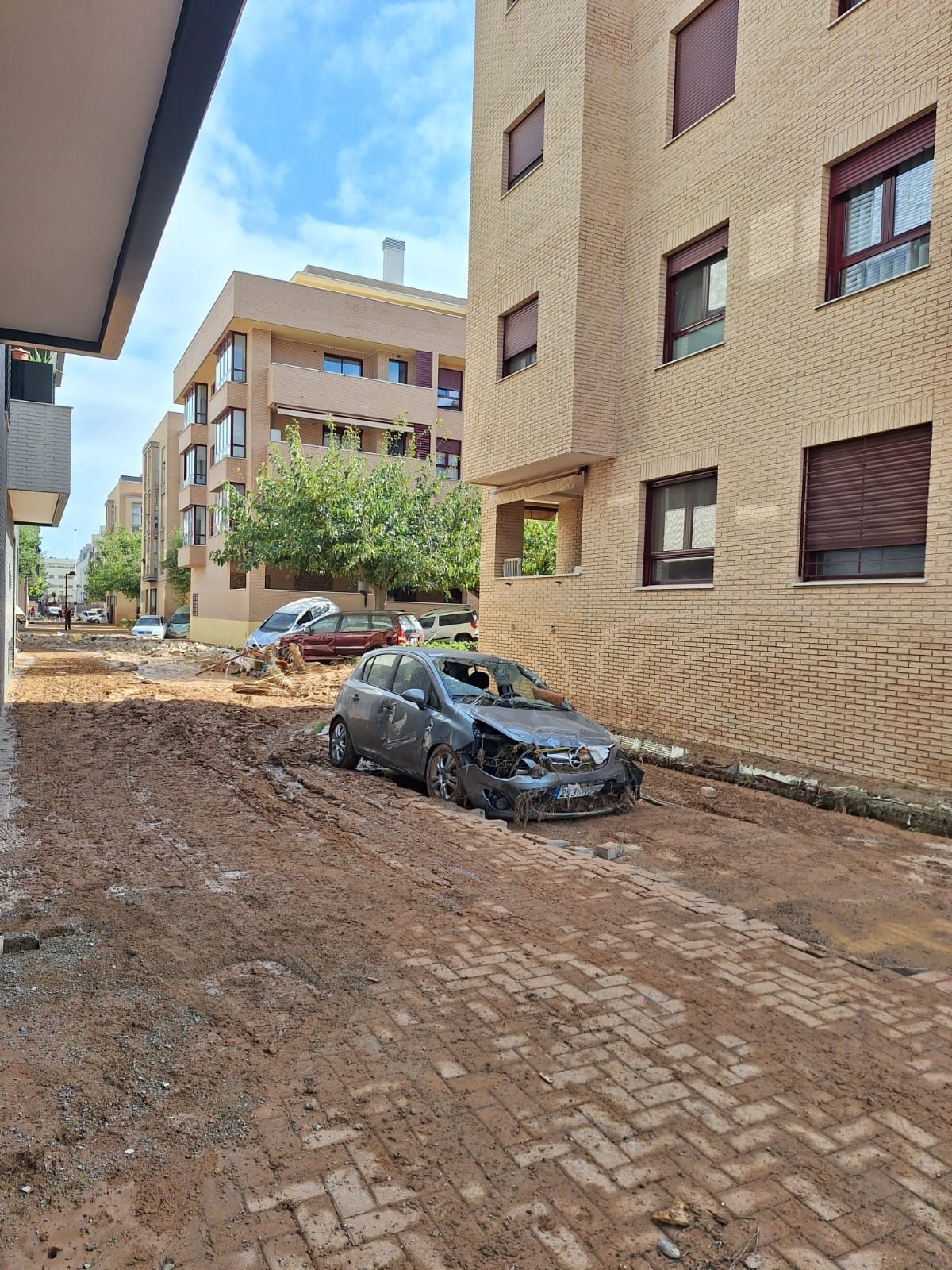 Calle de Paiporta cubierta de barro, con un coche destrozado junto a un edificio de viviendas.