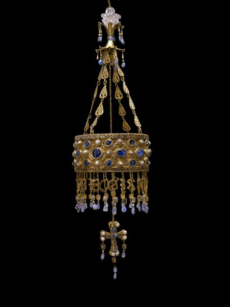 Corona de oro con piedras azules de la que cuelgan letras y una cruz
