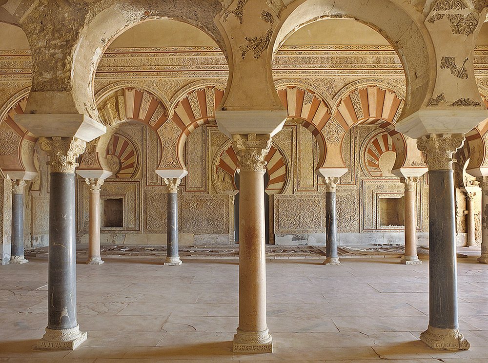 Sala con arcos de herradura de dovelas rojas y blancas y muros cubiertos de relieves vegetales